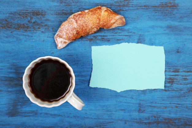 Composición de café croissant recién hecho y tarjeta de papel sobre fondo de madera