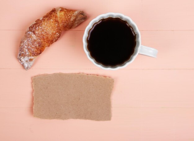 Composición de café croissant recién hecho y tarjeta de papel sobre fondo de madera