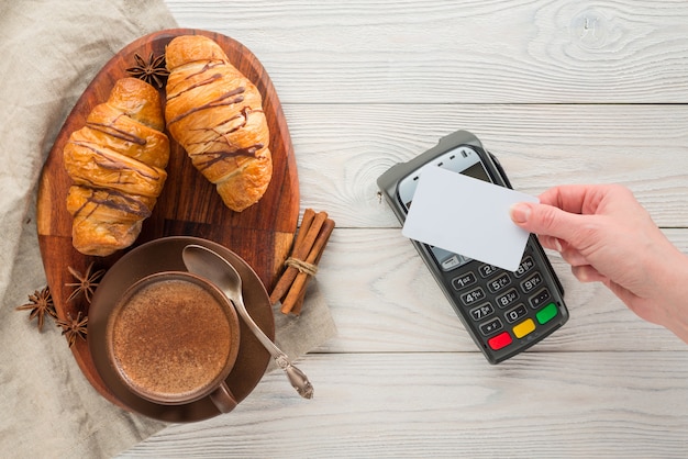 Composición de café y croissants con terminal de pago bancario sobre un fondo de madera