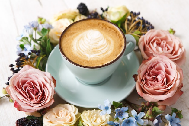 Composición de capuchino y flores. Taza de café azul con espuma cremosa, flores frescas y secas