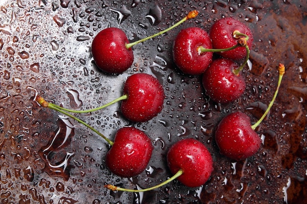 Composición de cerezas dulces sobre un fondo oscuro con vista superior de gotas de agua. Cerca de grandes cerezas rojas