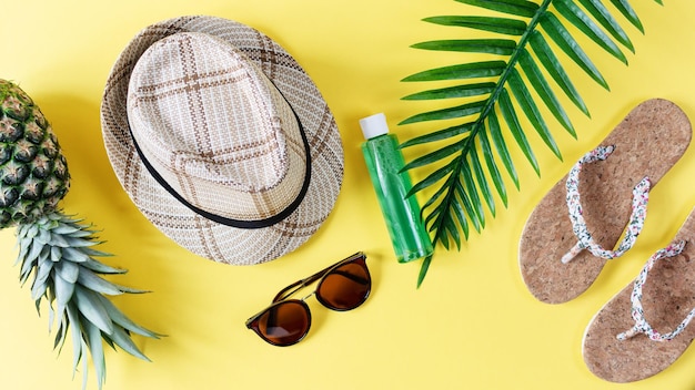 Composición colorida de verano con sombrero de paja, gafas de sol, hojas de palma, piña y chanclas.