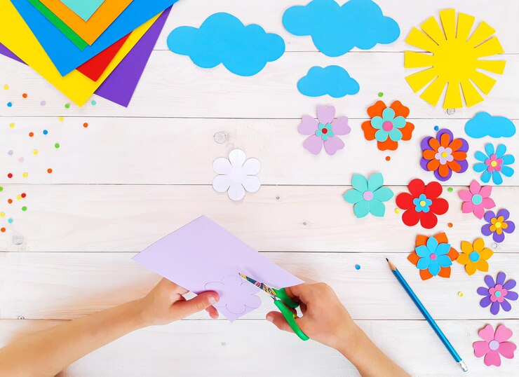 Foto composición de coloridas flores de verano, sol, nubes de papel multicolor, paso a paso. el niño hace manualidades con sus propias manos. bonita creatividad artística hecha a mano en una mesa de madera. vista superior, espacio de copia