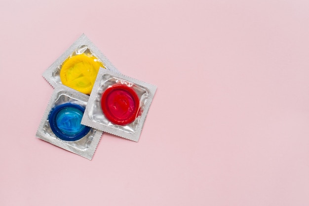 Foto composición con condones de colores sobre superficie rosa pastel. concepto anticonceptivo y sexo seguro