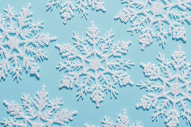 Composición de copos de nieve de brillo blanco sobre un fondo azul pastel