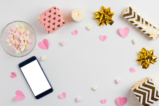 Composición de corazones rosas hechos de papel, regalos, un teléfono y malvaviscos en forma de corazón.