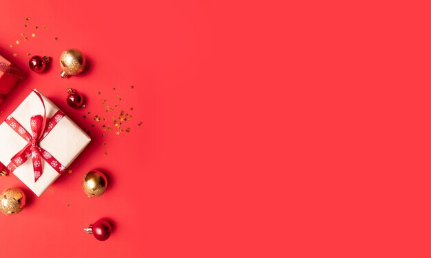 Composición creativa con caja roja presente, cintas, bolas grandes y pequeñas de oro rojo, decoraciones navideñas en rojo.