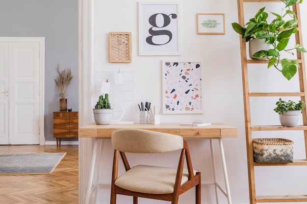 Composición creativa de diseño de interiores de oficina en casa con estilo escandinavo con marcos, escritorio de madera, silla, plantas y accesorios. Paredes neutras, suelo de parquet.