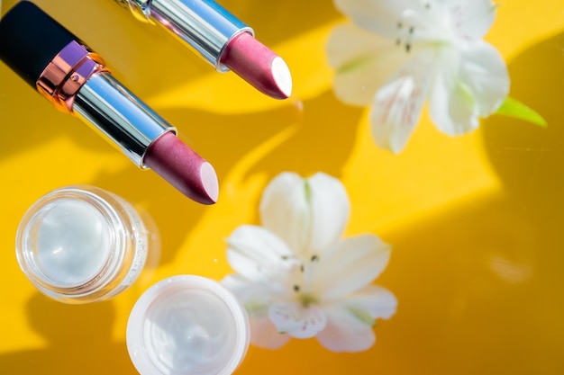 Composición creativa de lápices labiales rosas y flores blancas sobre un fondo amarillo brillante a la moda y a la moda