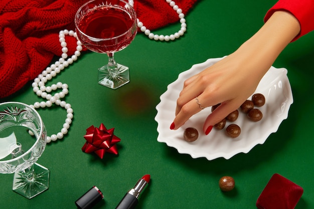 Composición creativa de Navidad año nuevo con manos de mujer y copa de champán rojo en mesa verde