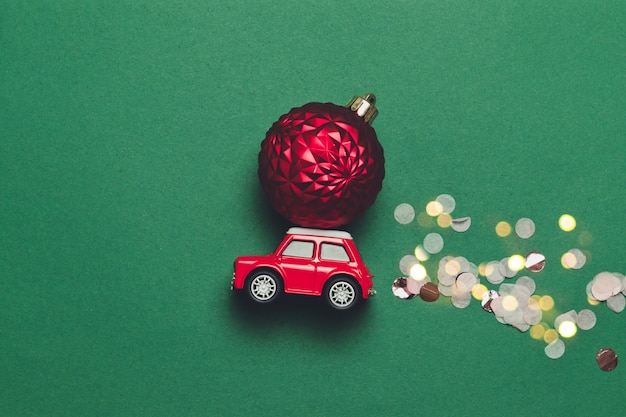 Composición creativa de Navidad con un coche de juguete rojo con una bola de Navidad en el capó y destellos dulces sobre un fondo verde con compise. Lay Flat, estilo minimalista