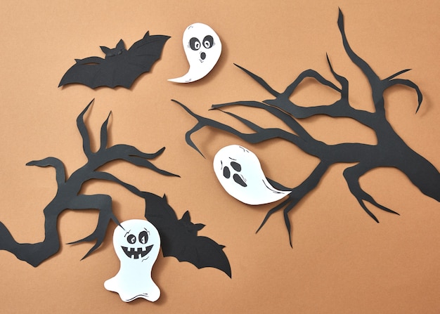 Foto composición creativa de papel con murciélagos voladores y fantasmas sobre ramas de árboles sobre un fondo marrón con espacio para texto. diseño artesanal para halloween. endecha plana