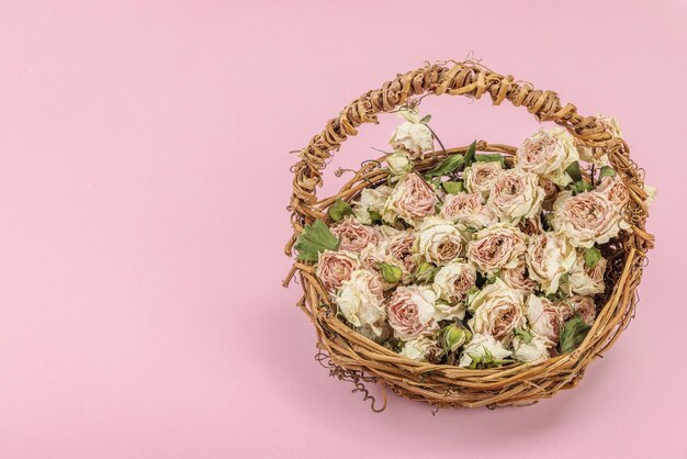 Composición creativa con rosas secas y delicadas en una canasta de mimbre casera Tarjeta de felicitación de fondo rosa pastel