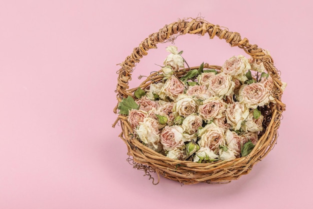 Composición creativa con rosas secas y delicadas en una canasta de mimbre casera Tarjeta de felicitación de fondo rosa pastel