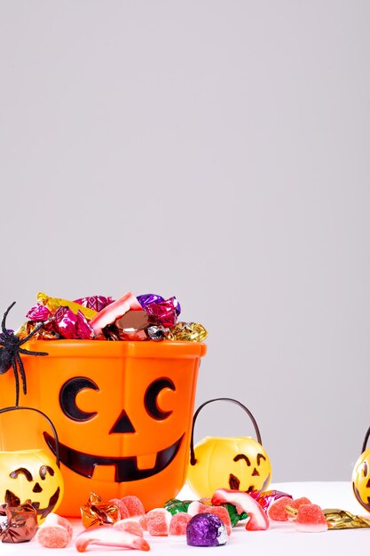 Foto composición del cubo de halloween con dulces de truco o trato, arañas y calabazas sobre fondo blanco. concepto de tradición y celebración de halloween.
