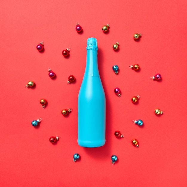 Composición de decoración de botella pintada de azul sobre un fondo rojo cubierto de vidrio colorido bolas de Año Nuevo con espacio de copia. Tarjeta de felicitación navideña
