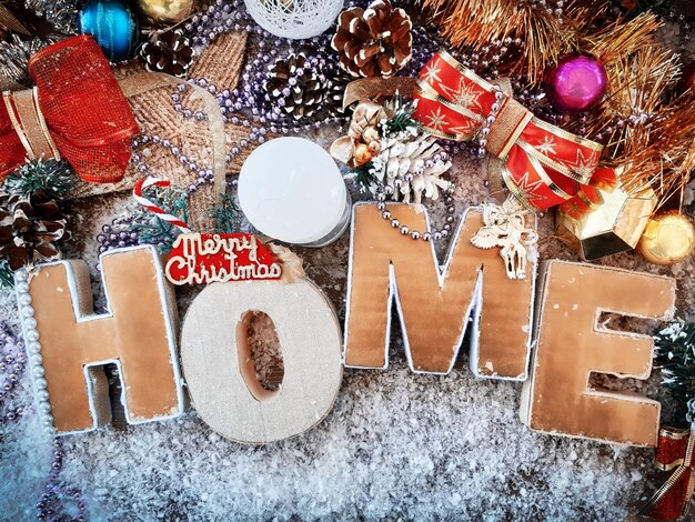 Composición decorativa de Navidad y año nuevo. La inscripción "Hogar", estrella, conos, velas, juguetes navideños, arcos sobre una mesa de madera con nieve. Vista superior, fondo para su diseño.