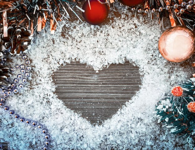 Composición decorativa de Navidad y año nuevo. Juguetes de Navidad, conos en una mesa de madera con nieve. En forma de corazón sobre una mesa en la nieve. Vista superior, fondo con espacio para copiar su texto.