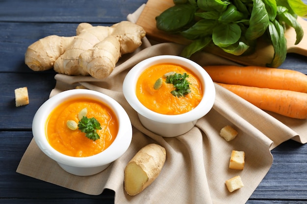 Composición con deliciosa sopa de zanahoria, hojas de albahaca y jengibre fresco sobre mesa de madera