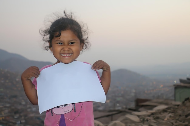 Composición para el Día del Niño. Chica sosteniendo una hoja de papel en blanco para insertar un texto o mensaje