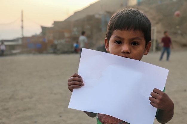 Composición para el Día del Niño. Niño sosteniendo una hoja de papel en blanco para insertar un texto o mensaje