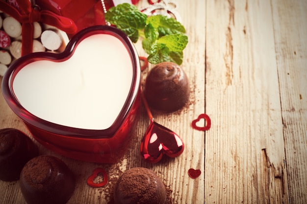 Composición del día de San Valentín con caramelos de chocolate, velas y corazones en la superficie de madera vintage. Foto tonificada con espacio para copiar texto