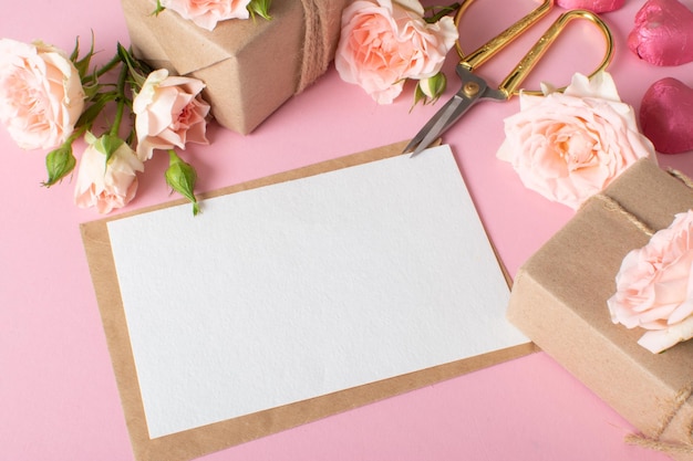 Una composición del Día de San Valentín de regalos ecoempaquetados, un sobre kraft y flores frescas sobre un fondo rosa claro, pancarta vintage