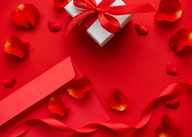 Composición del día de san valentín con sobre rojo, pétalos y caja de regalo