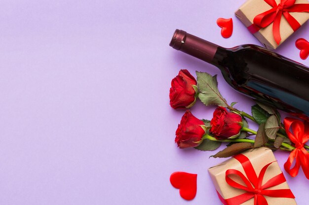 Composición para el día de San Valentín con vino rojo, flor de rosa y caja de regalos en la mesa.