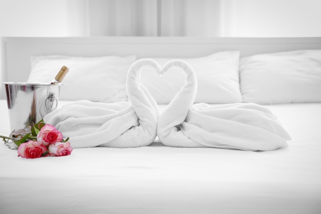 Composición de dos flores de cisnes de toalla y cubo de hielo con champán en la cama en la habitación del hotel