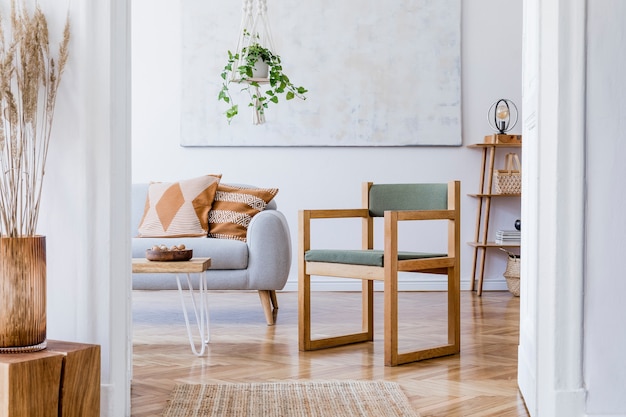 Composición elegante del interior del apartamento espacioso creativo con sofá gris, mesa de café, plantas, almohadas, alfombras y hermosos accesorios. Paredes blancas y suelo de parquet.