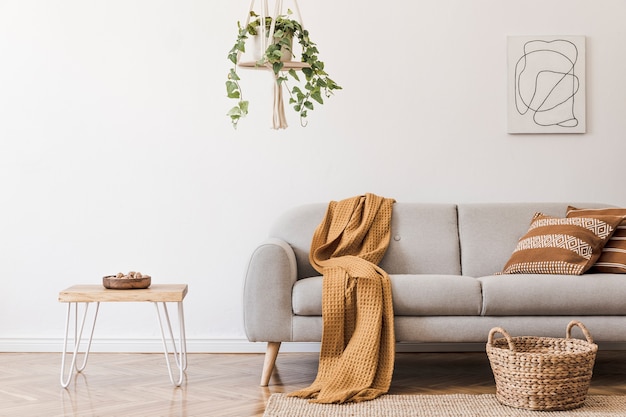 Composición elegante del interior de la sala de estar creativa y acogedora con sofá gris, mesa de café, plantas, alfombras y hermosos accesorios. Paredes blancas y suelo de parquet.