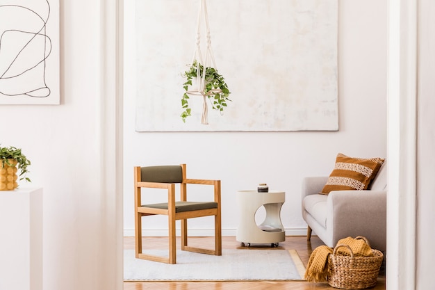 Composición elegante del interior de la sala de estar espaciosa creativa con silla, plantas, alfombras, pinturas y accesorios. Paredes blancas y suelo de parquet.