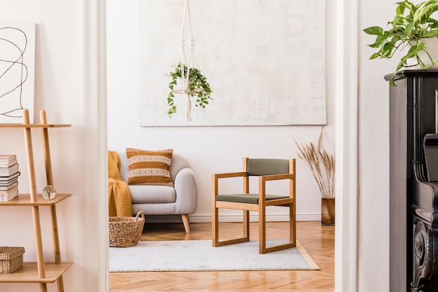 Composición elegante del interior de la sala de estar espaciosa creativa con sofá gris, silla, plantas, alfombras, pinturas y accesorios.