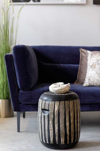 Foto composición elegante en el interior de la sala de estar con taburete de cerámica de diseño, sofá de terciopelo, almohadas, plantas, bandeja de mano y elegantes accesorios personales en concepto moderno.