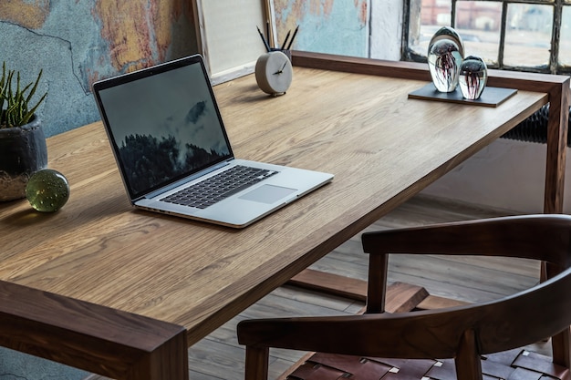 Composición elegante y moderna del interior del espacio de trabajo creativo con mesa y silla de madera, plantas y accesorios. Amplia habitación con paredes creativas y suelo de parquet.