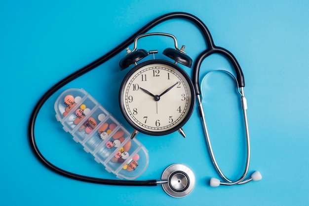 Composición con estetoscopio médico, reloj despertador y pastillas en azul