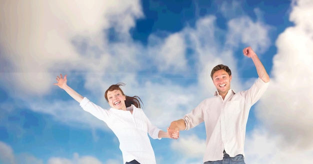 Composición de la feliz pareja celebrando, tomados de la mano saltando en el aire sonriendo, sobre el cielo azul