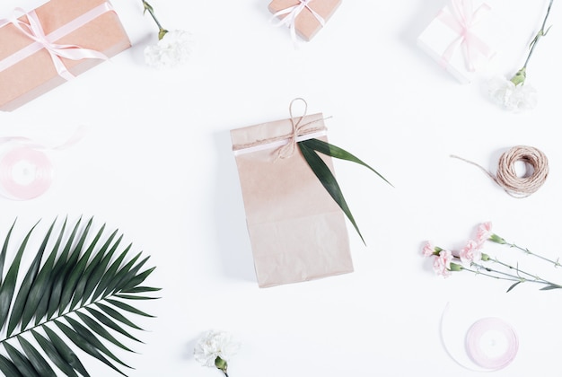 Foto composición festiva: cajas con cintas, bolsa de papel con un regalo y flores en la mesa blanca