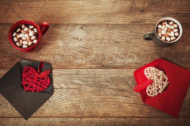 Composición festiva sobre mesa de madera rústica, taza roja y gris con malvaviscos o cacao, corazones en sobres, flores de rosas secas. Copie el espacio. Cumpleaños, Madre, San Valentín, Mujer, Día de la boda concepto