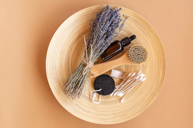 Composición flatlay con flores de lavanda y productos cosméticos naturales. Cosmética SPA ecológica. Suero facial, aceite esencial, cepillo facial masajeador, esponja, sal marina y palitos de bambú en placa de madera.