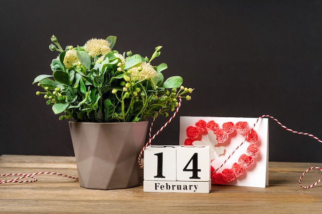 Composición de flores con corazones para el día de San Valentín sobre un fondo rosa con un calendario de madera