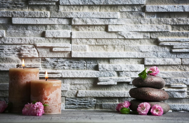 Composición de flores de guijarros de spa y velas sobre fondo de pared de ladrillo gris