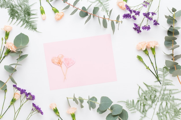 Composición de flores. Papel en blanco, flores de clavel, ramas de eucalipto sobre fondo pastel. Endecha plana, vista superior, espacio de copia