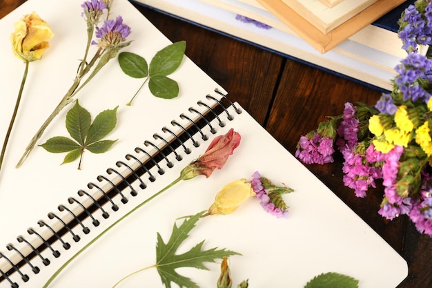 Composición con flores y plantas secas en el cuaderno en la mesa de cerca