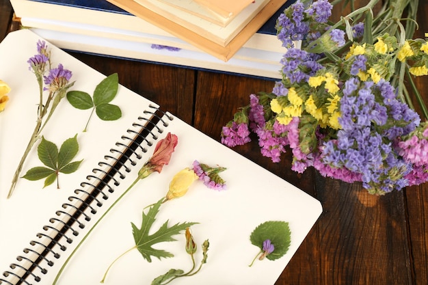 Composición con flores y plantas secas en cuaderno sobre fondo de madera