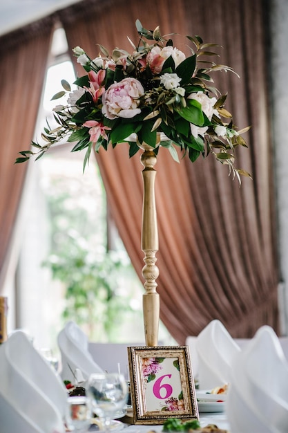 Una composición de flores y verde está en una mesa festiva en el salón de banquetes de bodas Stands sign number 6 Close up