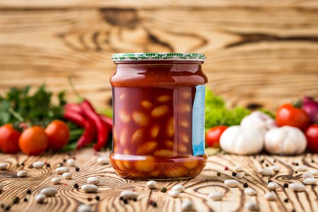 Composición de frijoles en escabeche con tomate en tarro e ingredientes sobre fondo de madera