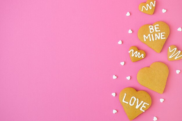 Composición con galletas caseras en forma de corazón de azúcar con palabras AMOR y SEA MÍO y muchos confeti de caramelo blanco con espacio para el texto sobre fondo rosa. Tarjeta de felicitación del día de San Valentín con espacio de copia