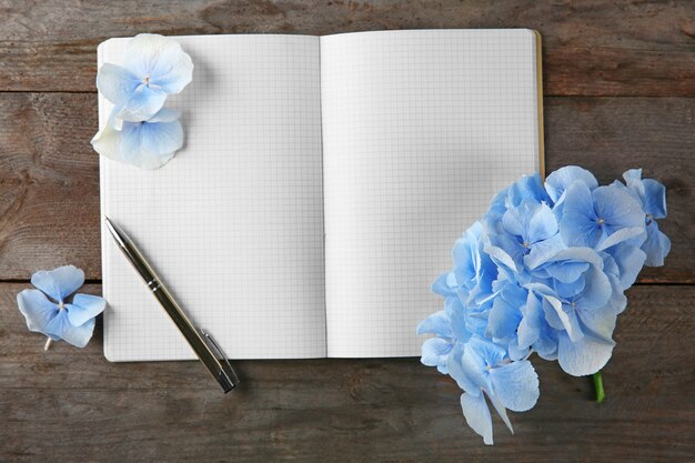 Composición con hermosas flores azules, cuaderno y bolígrafo sobre fondo de madera